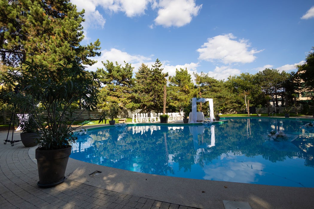 Piscina cu arcada decorata pentru cununie religioasa in aer liber si scaune albe pentru invitati, amenajate in gradina restaurantului