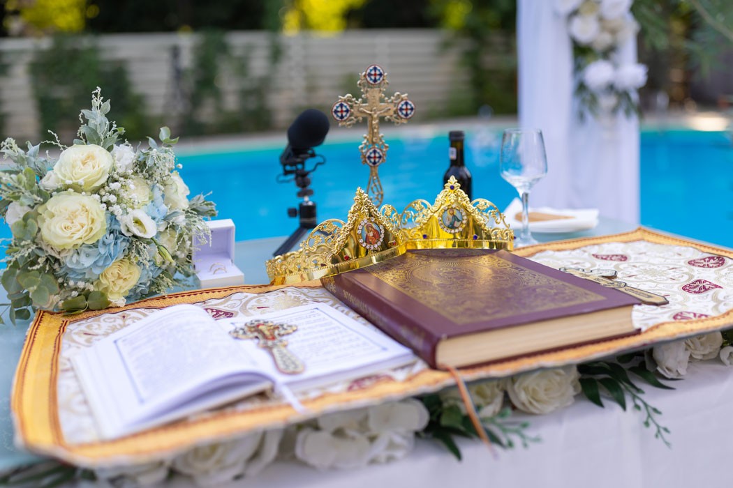 Cununii aurii de nunta, crucea si evanghelia aranjate pe masa, cu piscina in fundal, improvizatie pentru cununia religioasa in aer liber