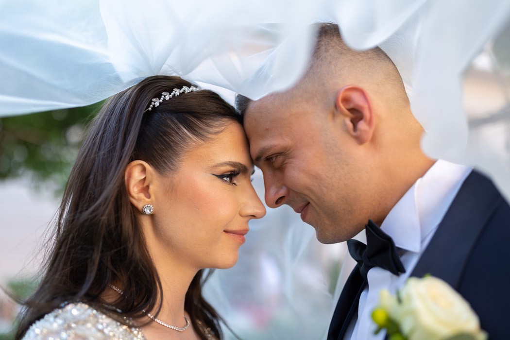 Mire si mireasa fata in fata sub voalul miresei portret apropiat realizat de fotograf la sedinta foto