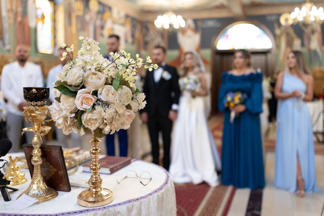 Flori, lumanare, cununii si Evanghelie pe tetrapod, cu mirii in fundal la cununia religioasa