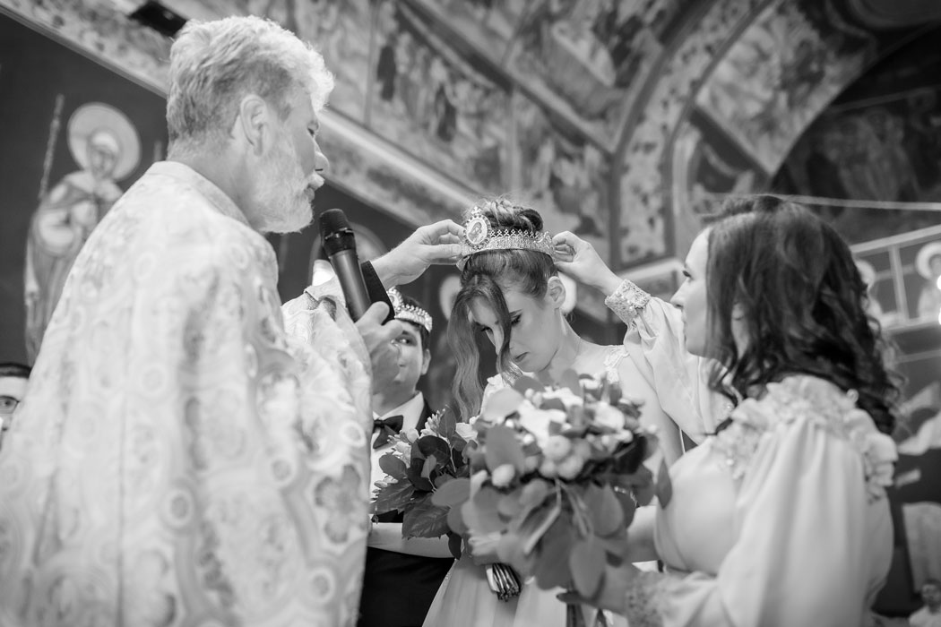 Preotul si nasa asezand cununia pe capul miresei in timpul ceremoniei religioase
