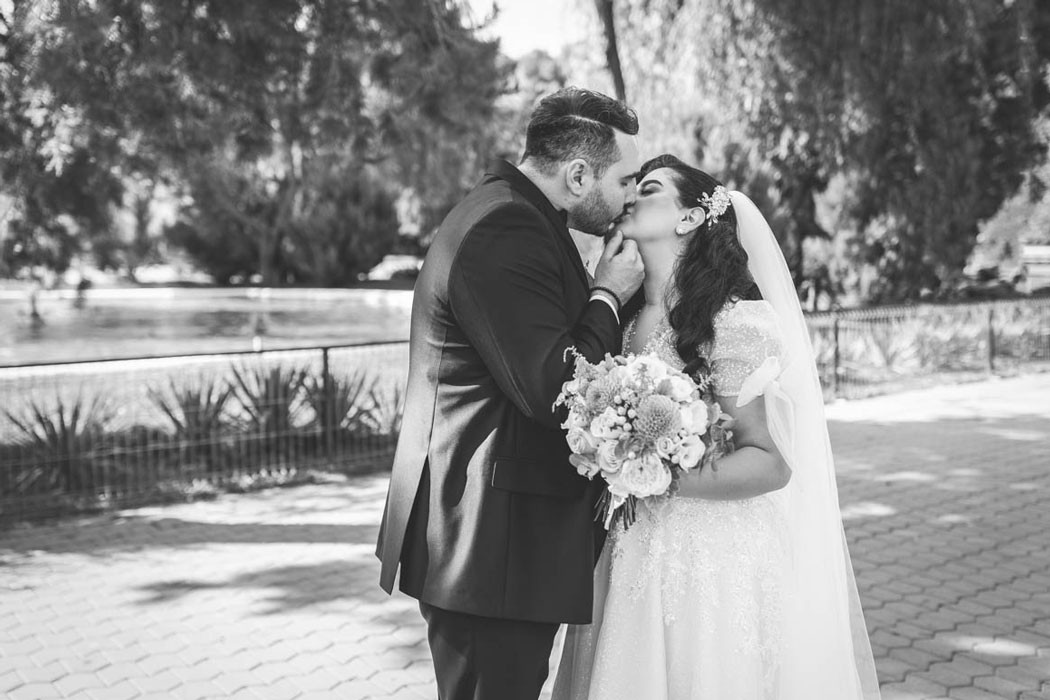 Fotografie portret alb-negru cu mirele sarutand mireasa in timpul sedintei foto de nunta in parc, cu lac si copaci in fundal