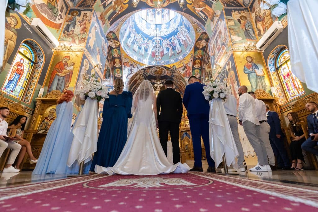 Fotografie din spate cu mirii, nasii, cavalerii si domnisoarele de onoare la cununia religioasa